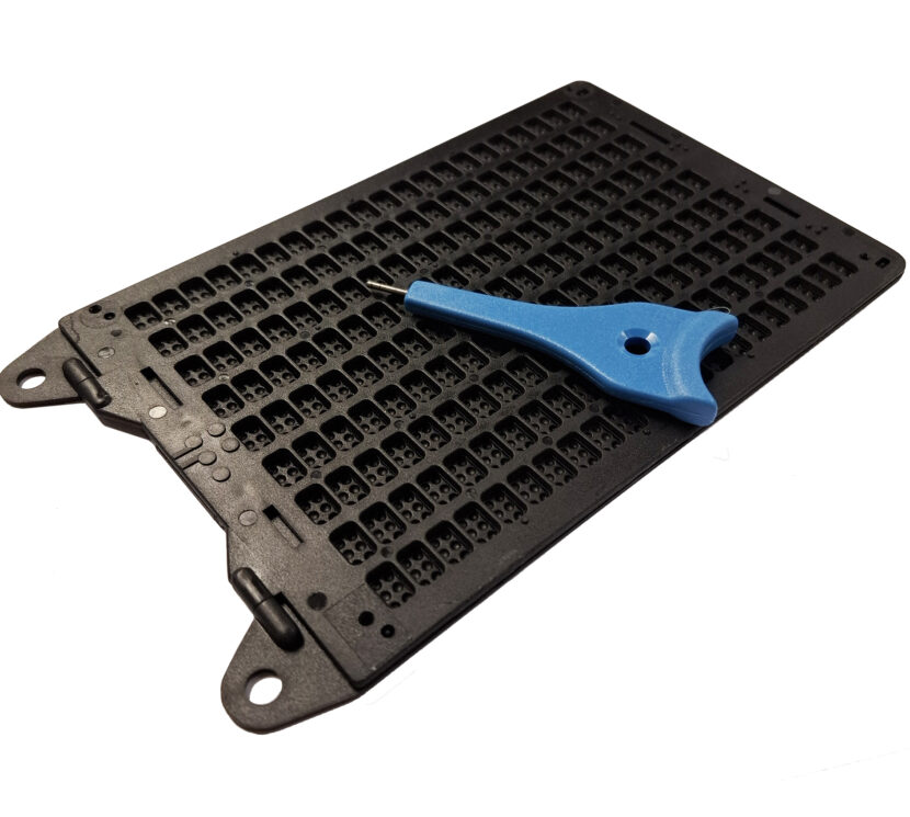 Musta, muovinen pistekirjoituskehikko ja sinivartinen metallikärkinen naskali.